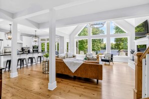 A spacious living area with a large window, a sofa, and a kitchen in the background. - Lakefront Lake Anna 5 Suites All Water Views (Mineral)