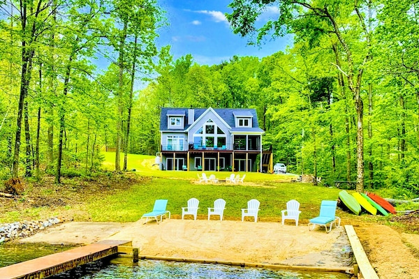 Spacious lakefront home with a private sandy beach, dock, and plenty of outdoor seating surrounded by lush trees