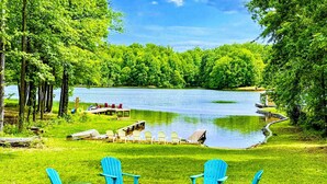 A lakeside view with a dock, chairs, and a fire pit.