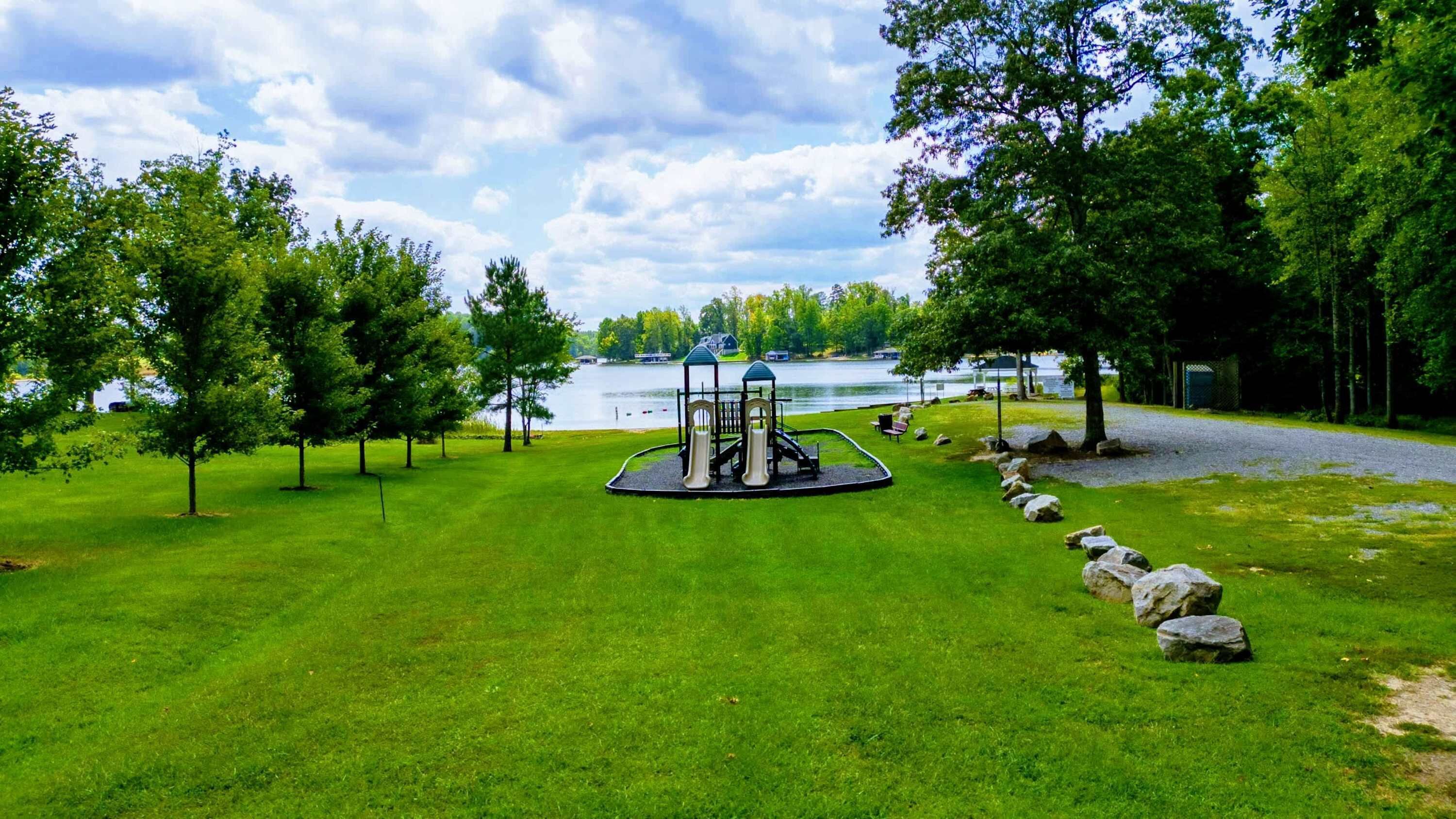 A playground with slides and a gazebo, surrounded by trees and a lake.
