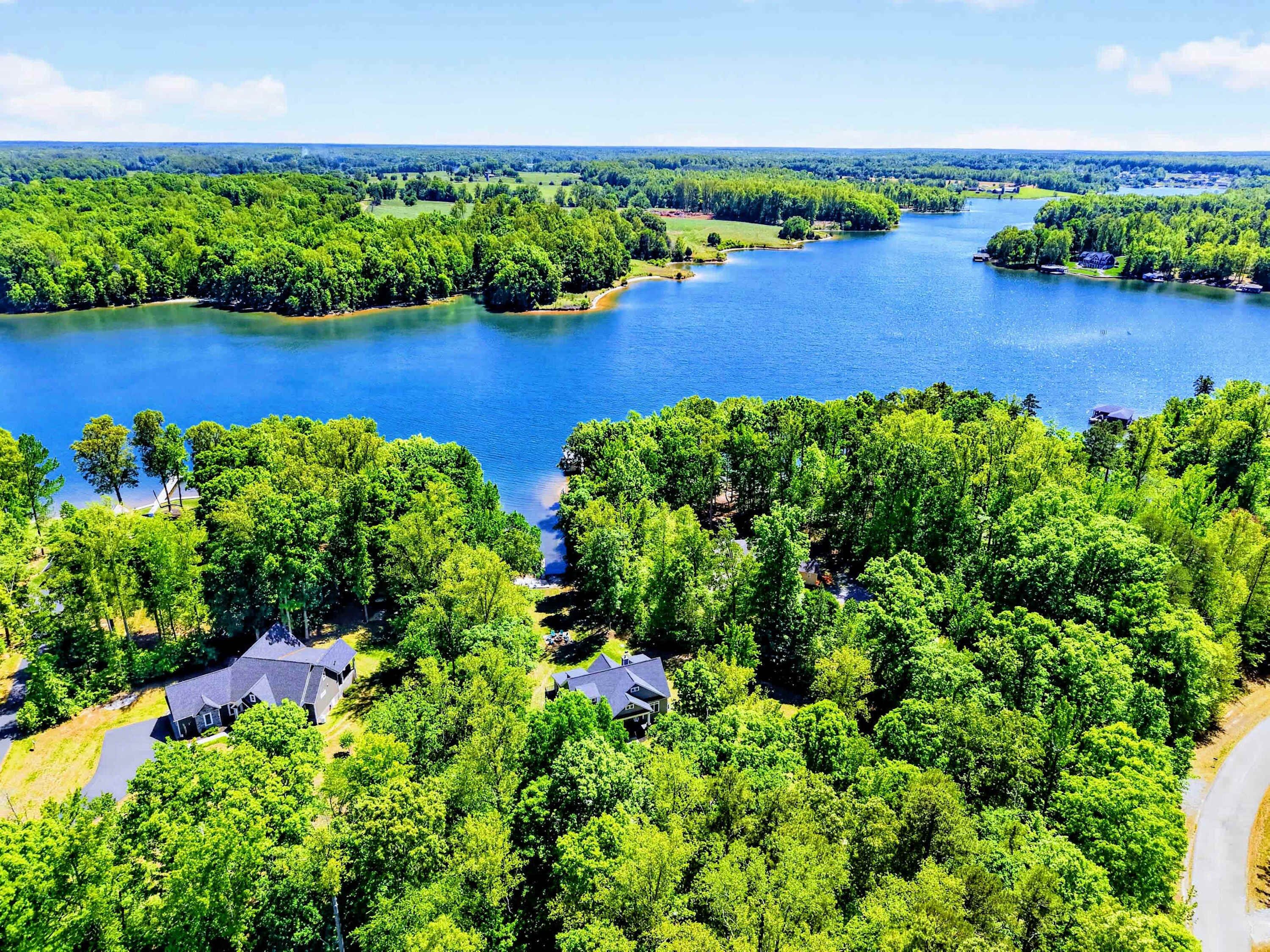 An aerial view of a lakeside property with multiple houses surrounded by dense greenery and a large body of water.