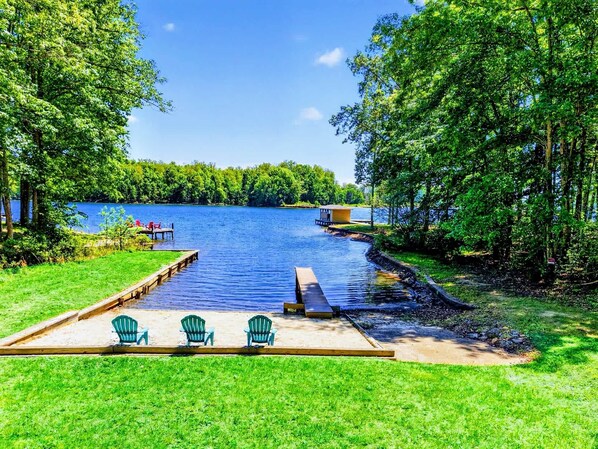 A lakeside deck with chairs and a small dock extending into the water.