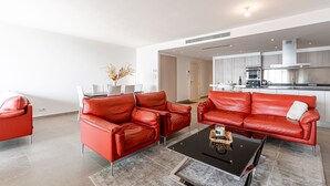 Un salon moderne avec des canapés en cuir rouge, une table basse noire et une cuisine en arrière-plan.