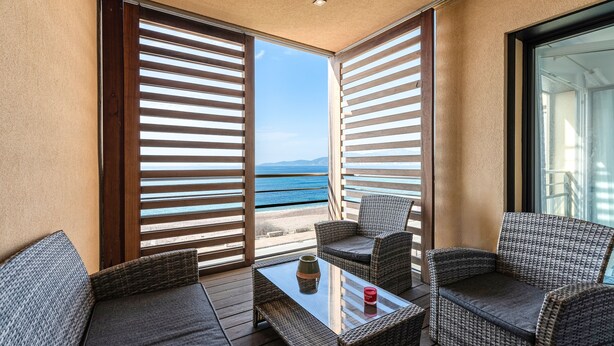 Un balcon agrémenté de meubles en osier, d’une table en verre et offrant une vue sur la mer.