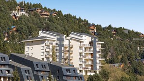 Un hotel de varios pisos con balcones, ubicado en una ladera rodeada de árboles.