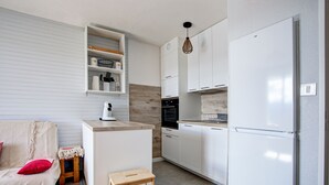 Una cocina compacta con armarios blancos, horno empotrado y refrigerador blanco.