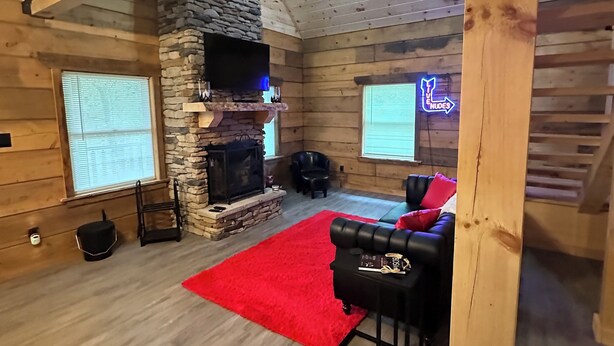 A log cabin interior with a stone fireplace, wooden beams, a red rug, and a leather sofa. -  ADULT ONLY Naughty Pines log cabin located in South Charleston, WV  (South Charleston)