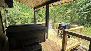 A covered deck with a hot tub, a barbecue grill, and a wooden deck railing. -  ADULT ONLY Naughty Pines log cabin located in South Charleston, WV  (South Charleston)