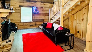 A cozy cabin interior with a fireplace, a red rug, a black leather sofa, and a wooden staircase. -  ADULT ONLY Naughty Pines log cabin located in South Charleston, WV  (South Charleston)
