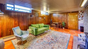 Ein Zimmer mit Holzwandverkleidung, einem grünen Sofa, einem gemusterten Teppich und einem Essbereich mit Tisch und Stühlen.
