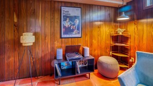 Ein Zimmer mit Holzwandverkleidung, einem 'Twin Peaks'-Poster, einer Plattenspieleranlage mit Lautsprechern, einem Bücherregal, einem blauen Sessel und einer Stehlampe.
