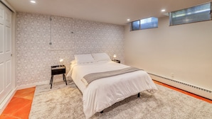 Ein Schlafzimmer mit strukturierter Tapete, einem Bett mit weißer Bettwäsche, einem Nachttisch mit Lampe und einem Fenster mit Blick.