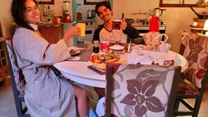 A dining area with a round table, chairs, and a kitchen in the background. - Villa Morena Benessere (Florianópolis)