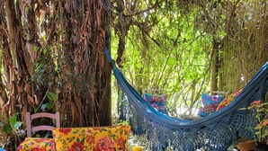 A hammock set up between trees, a wooden table with a tea set, and colorful cushions. - Villa Morena Benessere (Florianópolis)