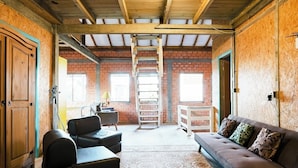 A spacious room with a loft area, a sofa, a chair, and a ladder leading to the loft. - Villa Morena Benessere (Florianópolis)