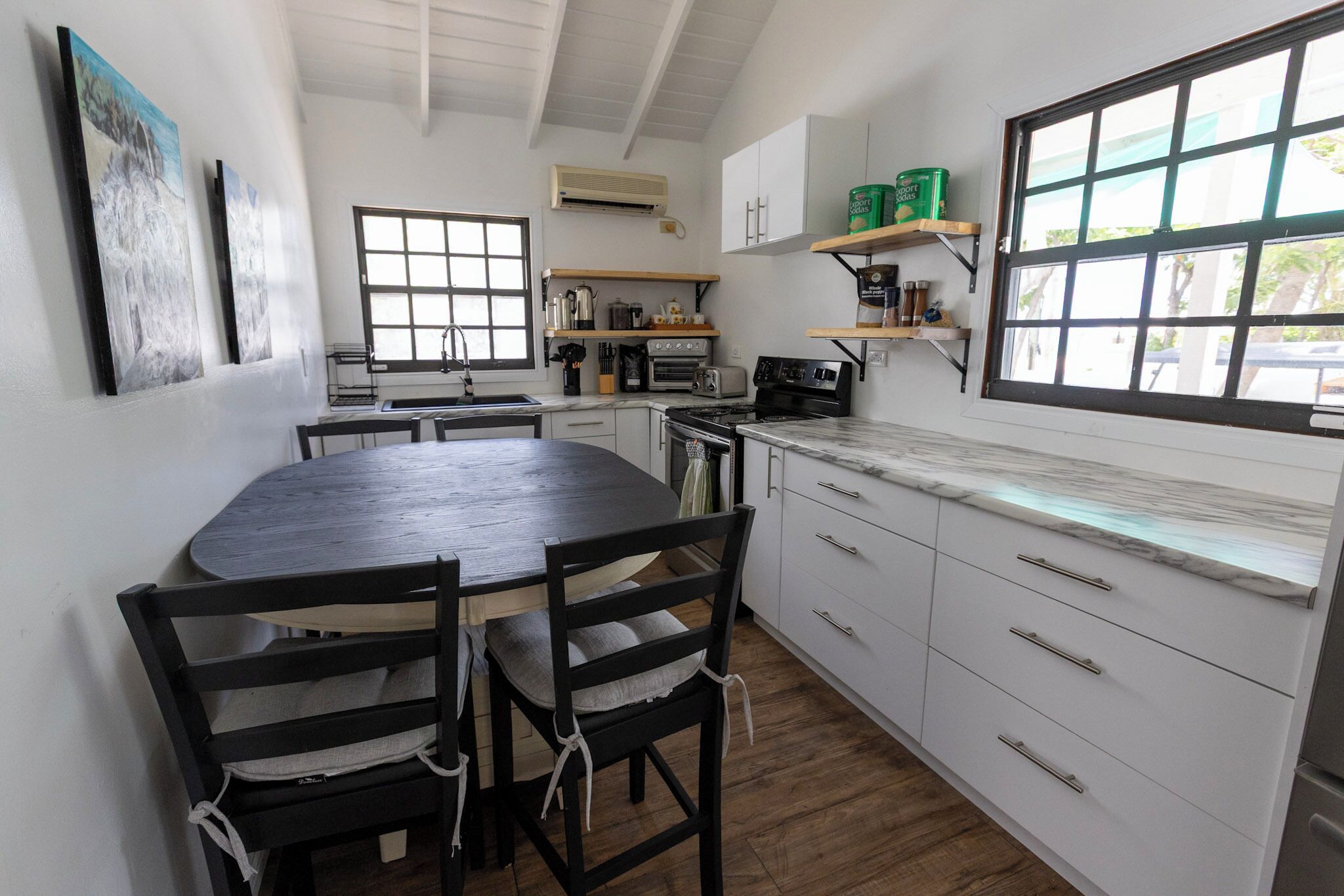 A compact kitchen with a round dining table, wooden chairs, a built-in oven, and a window with a view.