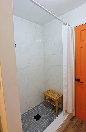 A bathroom with a shower, a wooden stool, and a tiled floor. - Potcake Villa — Stay with Purpose: Support Animal Welfare (cockburn town)