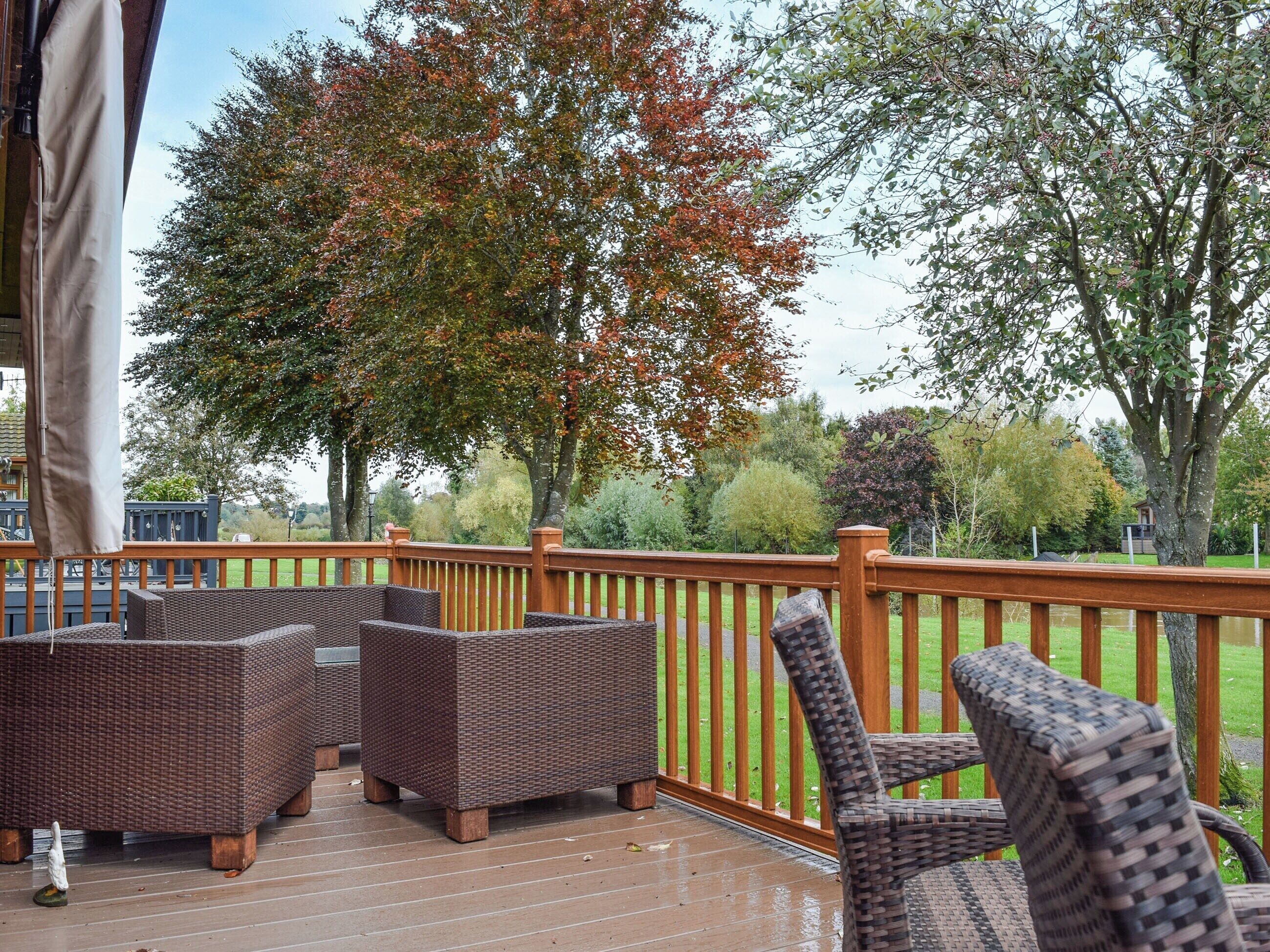A covered outdoor deck with wicker furniture and a wooden railing.