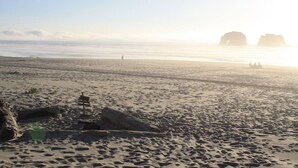 A beach with a wooden signpost, large rocks, and a distant view of the sea. - Dog-Friendly Oceanview Getaway Condo #9 (Rockaway Beach)