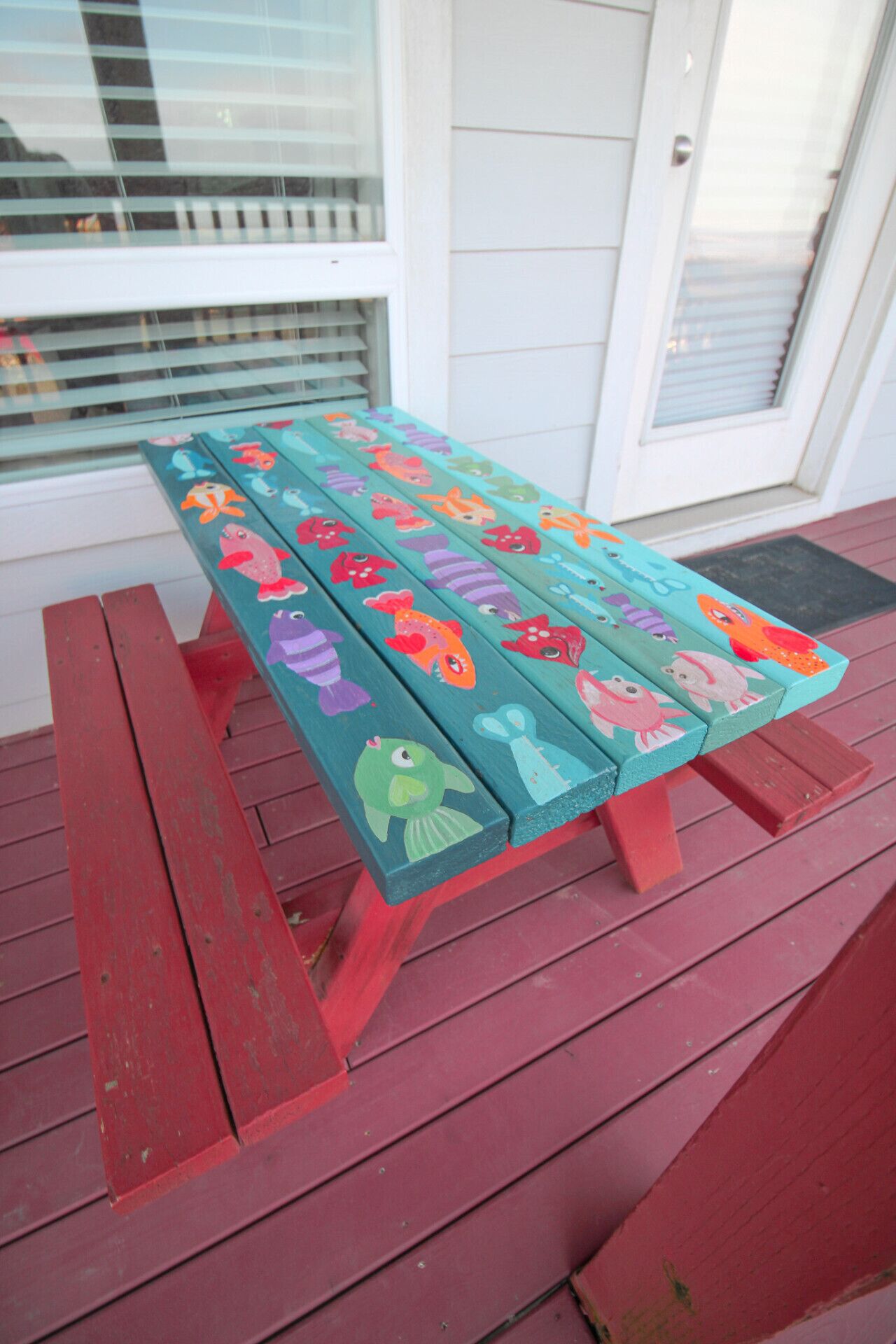 Een houten bankje met kleurrijke visjes, geplaatst op een rood terras.