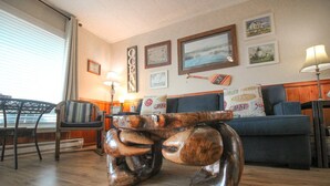 A living room with a wooden coffee table, a sofa, and a chair. There are framed pictures on the wall and a lamp on the side table. - Dog-Friendly Oceanview Getaway Condo #9 (Rockaway Beach)