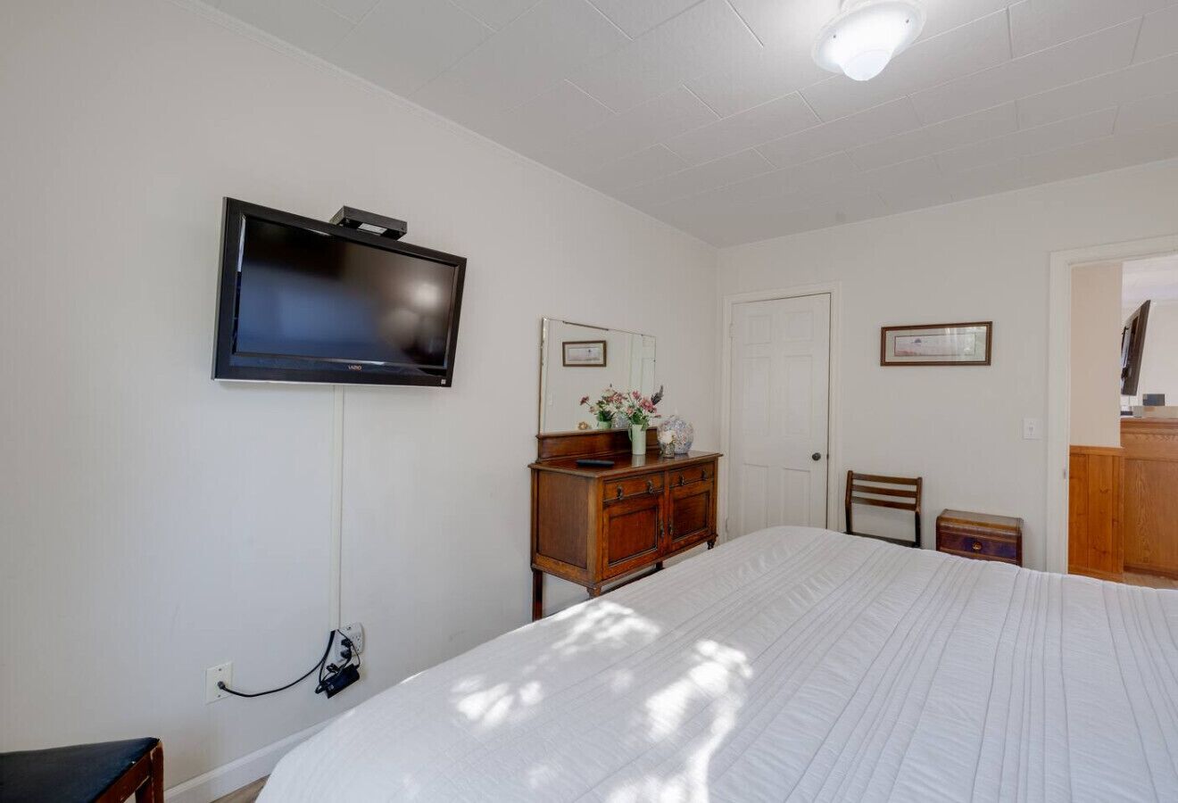 Une chambre à coucher comprenant un lit, une commode, un téléviseur fixé au mur et une porte.