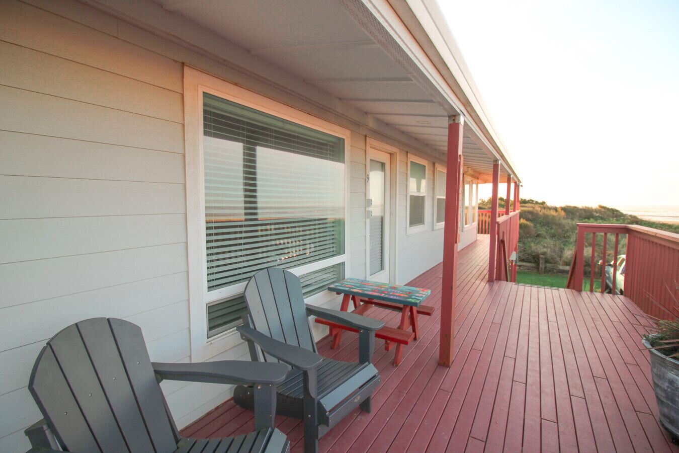 A covered porch with two Adirondack chairs and a picnic table, overlooking a grassy area.