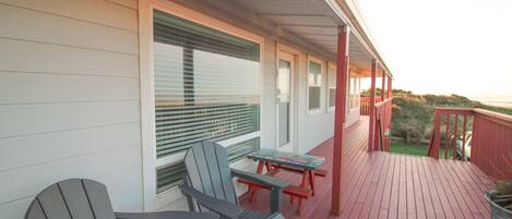 A covered porch with two Adirondack chairs and a picnic table, overlooking a grassy area.