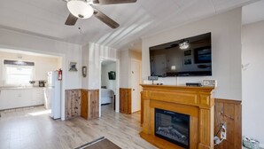 A spacious living room with a fireplace, a ceiling fan, and a large TV mounted above it. - Dog-Friendly Oceanview Getaway Condo #9 (Rockaway Beach)