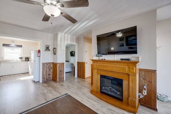 A spacious living room with a fireplace, a ceiling fan, and a large TV mounted above it.