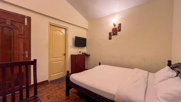 A bedroom with a wooden bed, a television mounted on the wall, and a door. - Sai Residency (Kodaikanal)