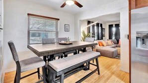 Un espace repas avec une table et des bancs en bois, un ventilateur de plafond et une fenêtre équipée de stores.