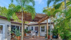 Une terrasse couverte avec une pergola, des sièges d’extérieur et des plantes en pot.