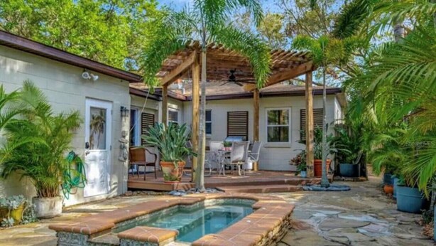 Une maison avec une piscine en pierre, du mobilier d’extérieur et des plantes en pot.