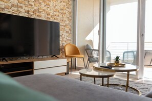 Relax in a stylish living space with a large flat-screen TV, comfortable seating area, and sliding glass door leading to a balcony with an outdoor view.