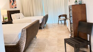 Una habitación de hotel con dos camas, un aparador de madera, una silla y un ventanal con cortinas.