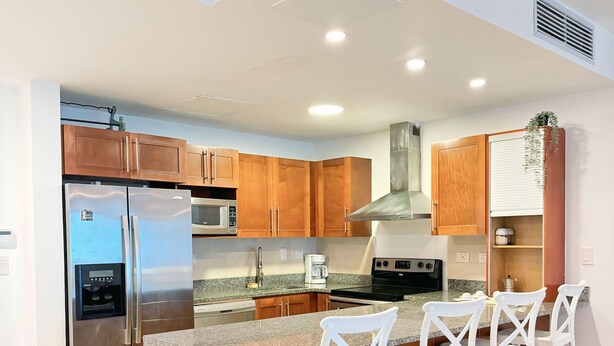 Una cocina moderna con un refrigerador de acero inoxidable, un microondas y una estufa. Cuenta con gabinetes de madera y una encimera de granito.