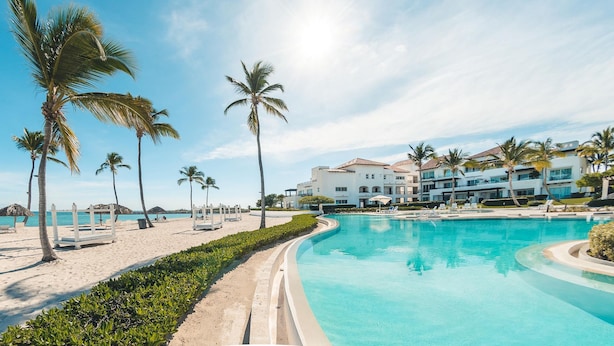 A resort with a swimming pool, palm trees, and beach chairs.