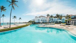 A swimming pool with lounge chairs, palm trees, and a building with multiple balconies.