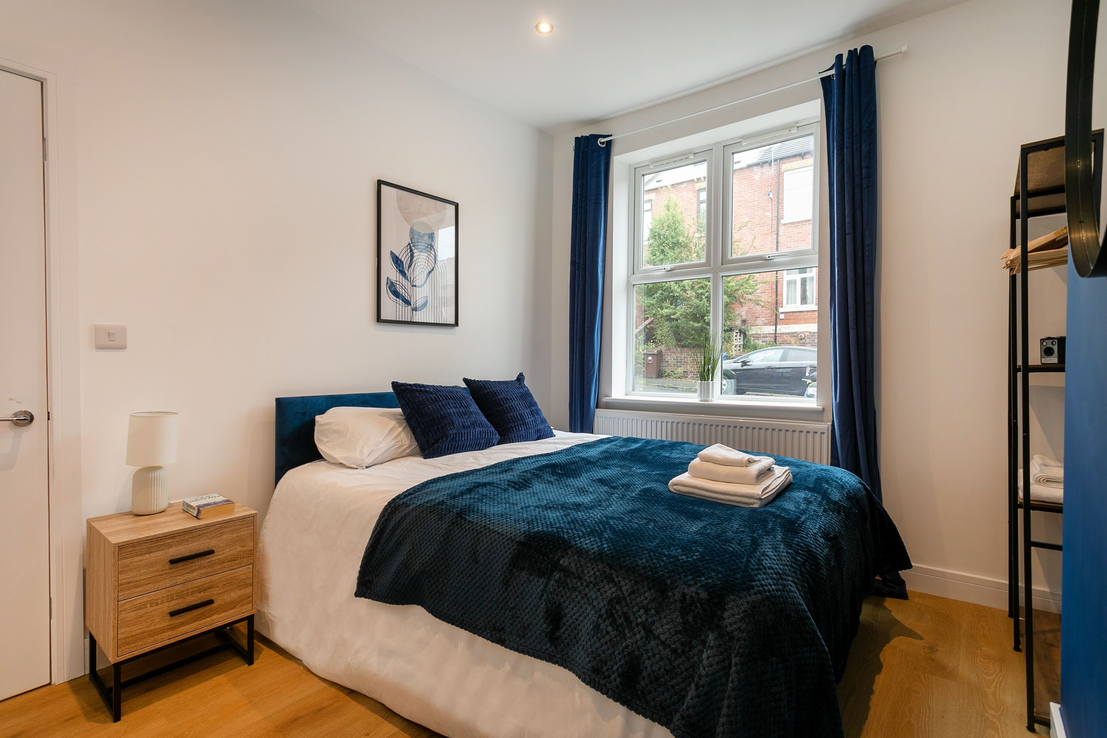 A bedroom with a bed, a nightstand, a window with curtains, and a radiator.
