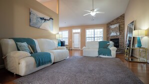 Ein geräumiges Wohnzimmer mit zwei weißen Sofas, einem großen grauen Teppich und einem Deckenventilator.