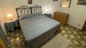 A bedroom with a bed, bedside lamps, a dresser, a mirror, and patterned floor tiles. - Villa Pino 150 meters from the sea and 5 min from Palermo airport area (Carini)