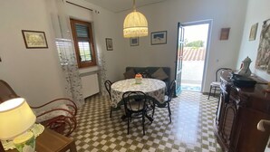 A dining area with a checkered floor, a round table with chairs, a hanging light fixture, and a window with blinds. - Villa Pino 150 meters from the sea and 5 min from Palermo airport area (Carini)