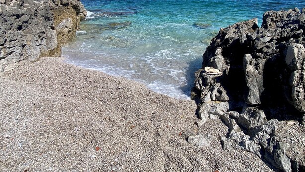 Une plage rocheuse avec une eau d’un bleu limpide et un rivage composé de petits galets.