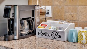 Una cafetera, una barra de café y una caja de cápsulas de café sobre una encimera de granito.
