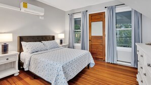 Un dormitorio con cama, mesitas de noche, cómoda, ventana con cortinas y ventilador de techo.