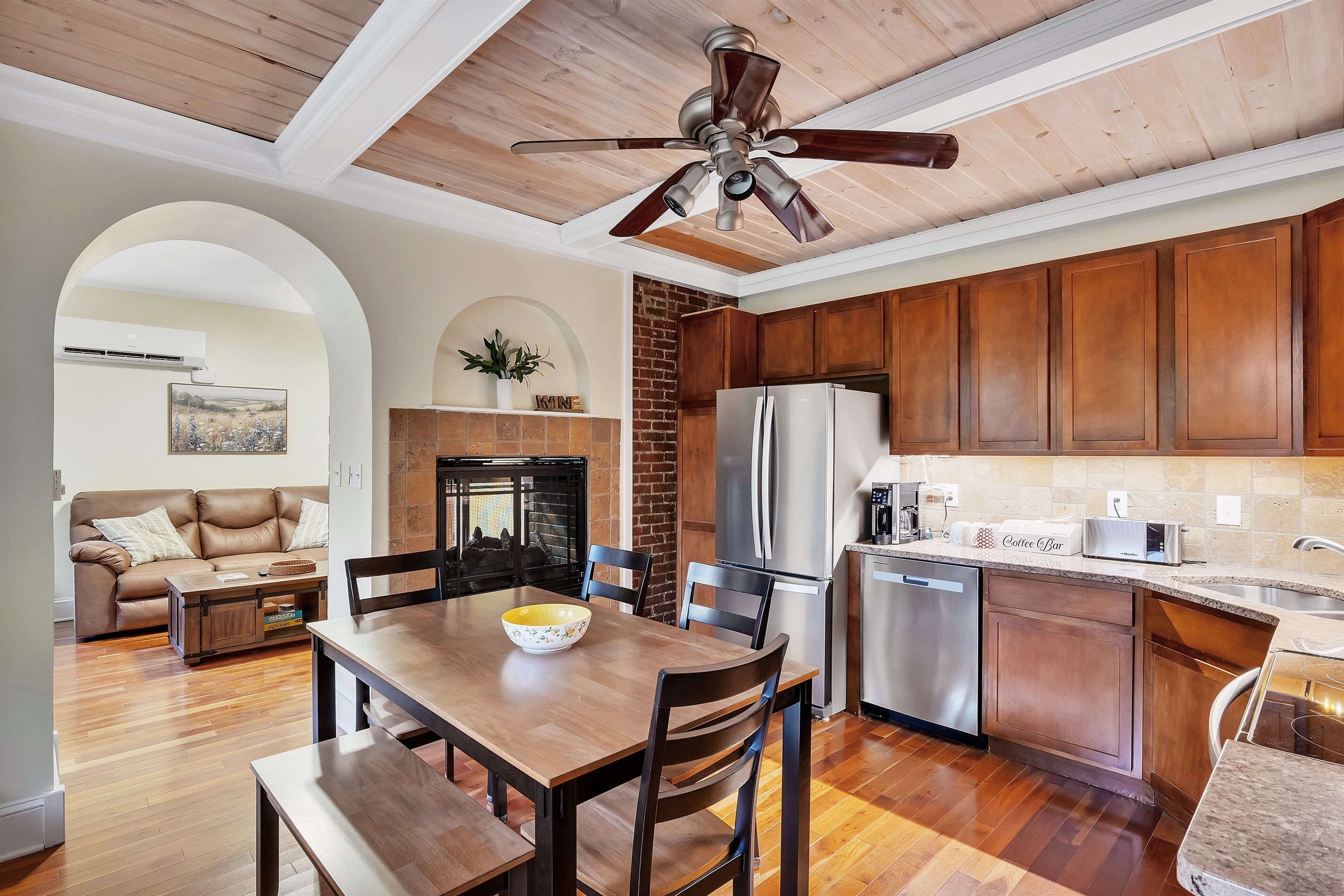 A modern kitchen with wooden cabinets, a stainless steel refrigerator, and a dining area with a wooden table and chairs.