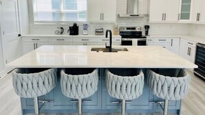 A modern kitchen with a large island, white cabinetry, and pendant lighting.