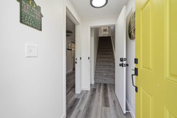 A hallway with a staircase leading to another room, a light switch, and a door.