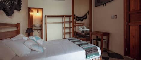 A neatly made bed with pillows and a blanket, a bedside table with a lamp, a wooden headboard, a TV mounted on the wall, and a checkered floor.
